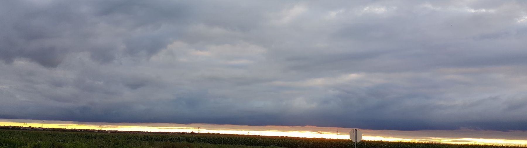Storm clouds over a band of gold light and a cornfield at the edge of Kyle, Texas
